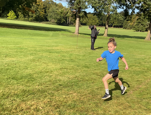 A child running on grass with a person behind her

Description automatically generated